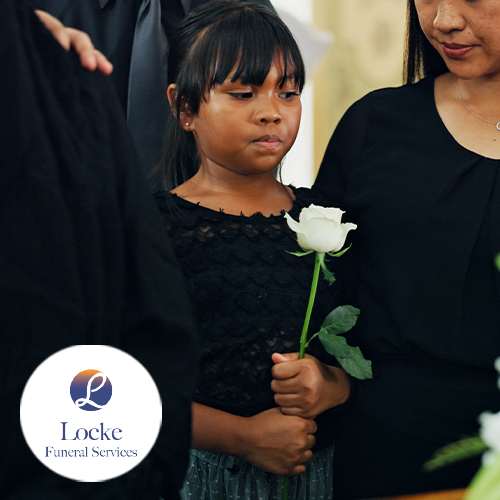 Child dressed in black clothing by a white rose at a funeral